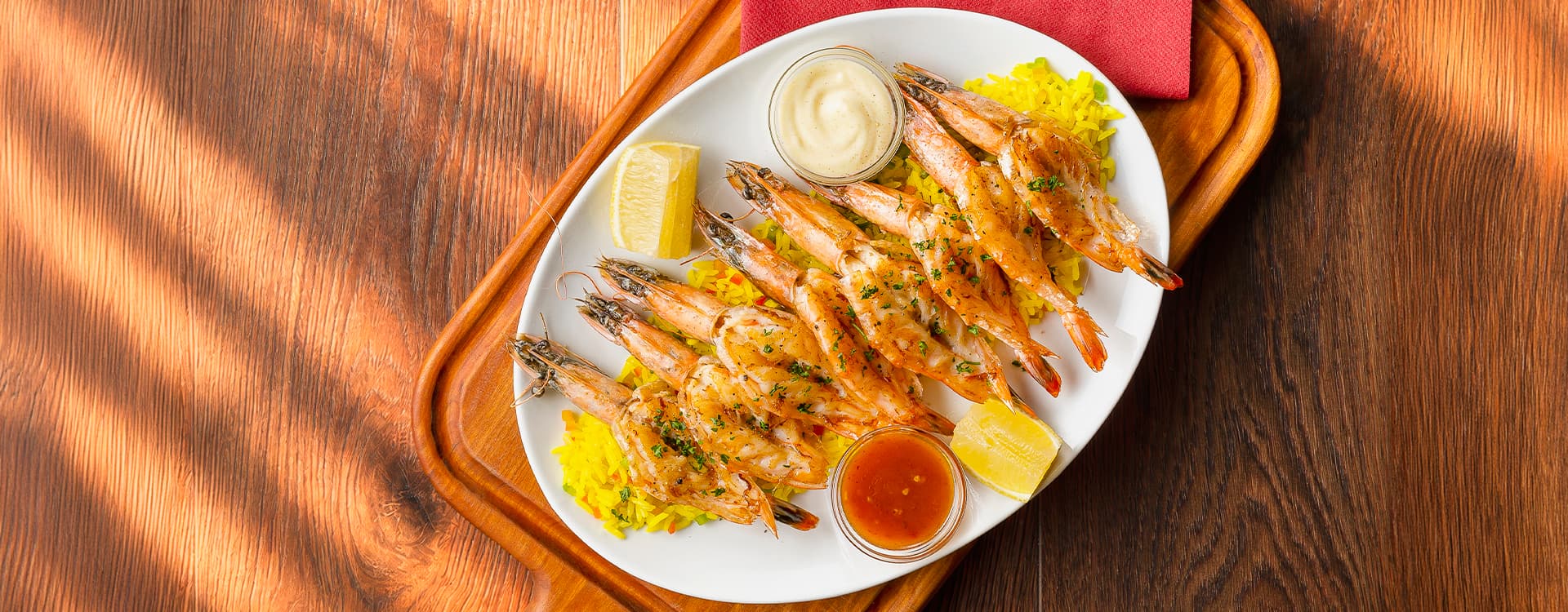 Grilled prawns topped with creamy garlic sauce and fresh chives, served on a baked potato with golden fries and a lemon wedge on a white plate