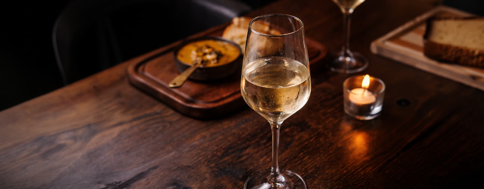 Chilled glass of white wine displayed on a wooden restaurant table with soft candlelight and blurred dining elements in the background