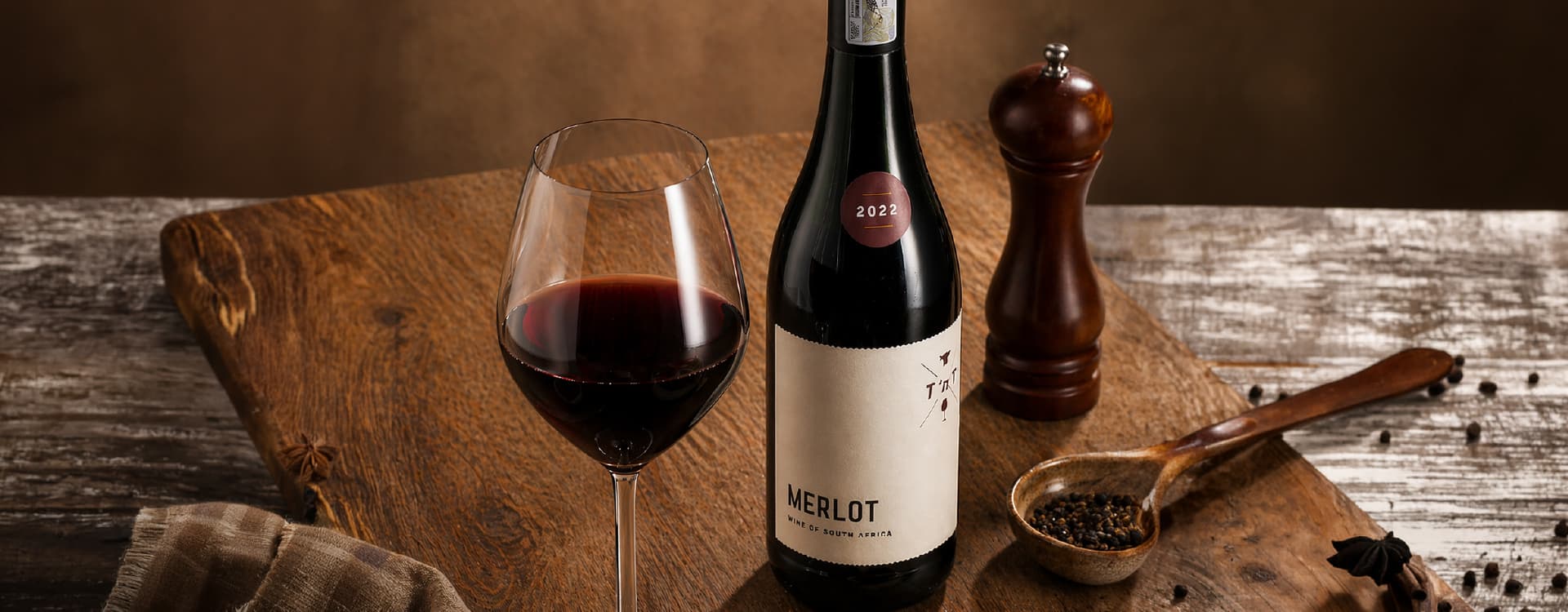 Bottle of South African Merlot wine and a glass of red wine displayed on a rustic wooden table