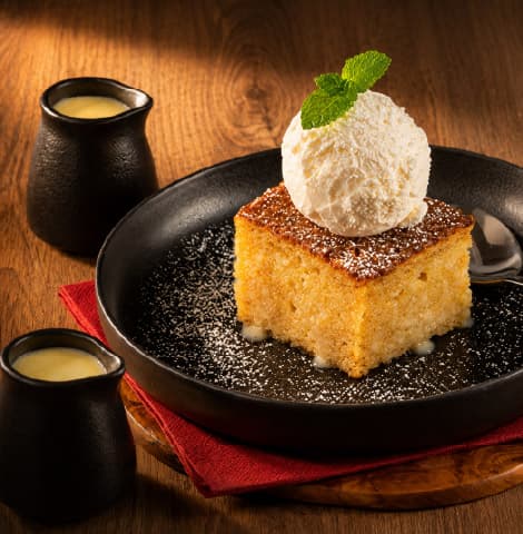 Traditional South African malva pudding dusted with powdered sugar and topped with a scoop of vanilla ice cream and fresh mint