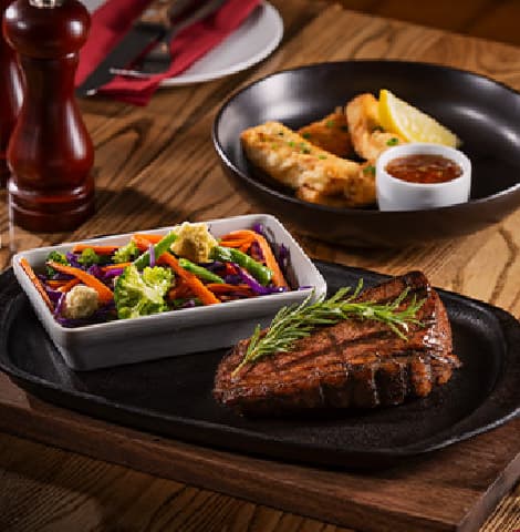 Char-grilled steak garnished with fresh rosemary, served on a sizzling platter with a colorful mixed vegetable medley
