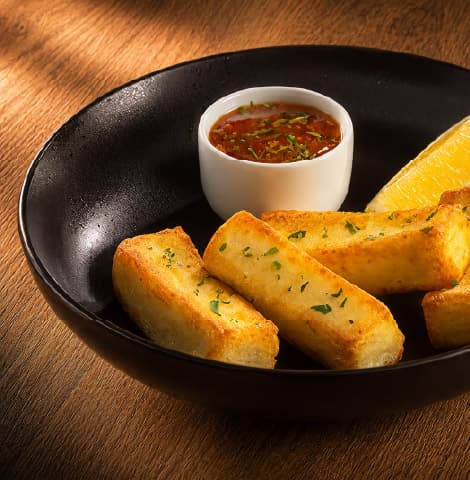 Fried halloumi slices garnished with herbs, served with a dipping sauce and a lemon wedge on a black appetizer plate