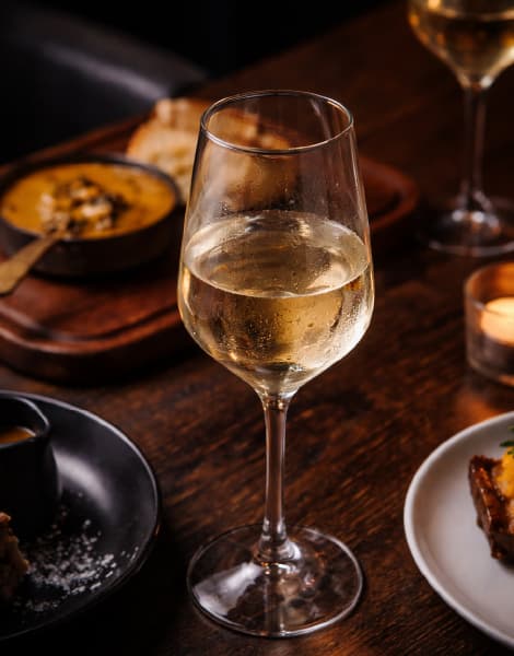 Chilled glass of white wine served on a rustic wooden restaurant table, surrounded by gourmet dishes